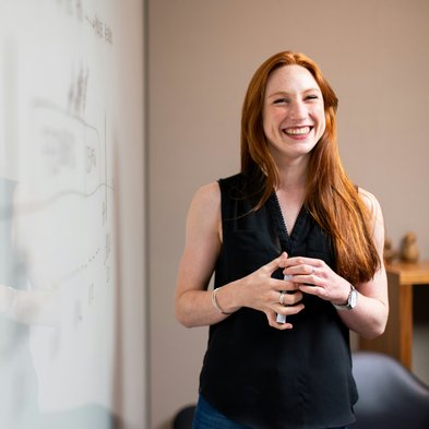 Frau in dunklem Oberteil neben Whiteboard